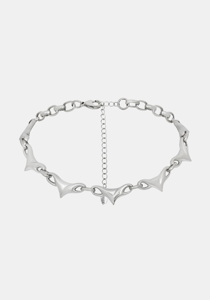 A silver-toned chain necklace featuring elongated, pointed spike links and a central extender chain, shown against a light gray background.