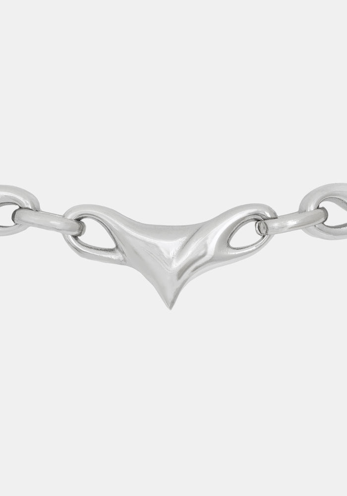 A close-up of a polished silver chain necklace featuring a distinctive central triangular clasp with looped details, set against a solid light gray background.