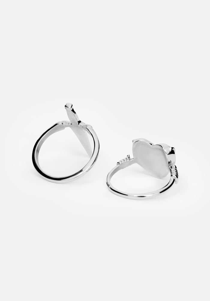 A pair of polished silver rings with heart and sword designs on the front and center of both rings against a white studio backdrop
