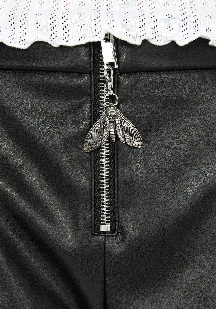 Close up of silver moth pendant on metal zip for faux leather micro shorts.