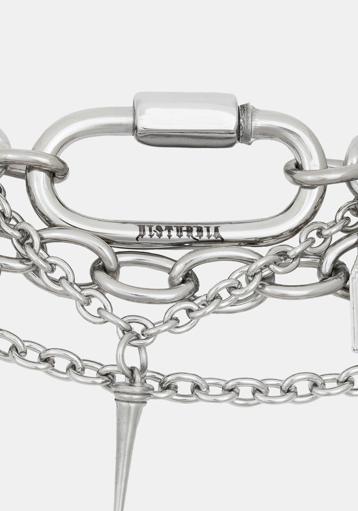Close-up of a silver-toned chain bracelet featuring a large oval carabiner clasp engraved with 'DISTURBIA', layered chain links, and a pointed spike charm, on a light gray background.