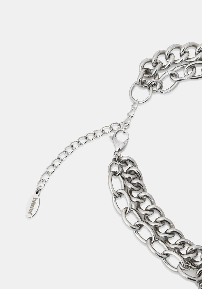 Close-up of a silver-toned chunky chain necklace with an adjustable extender chain and a small branded tag, photographed on a light gray background.