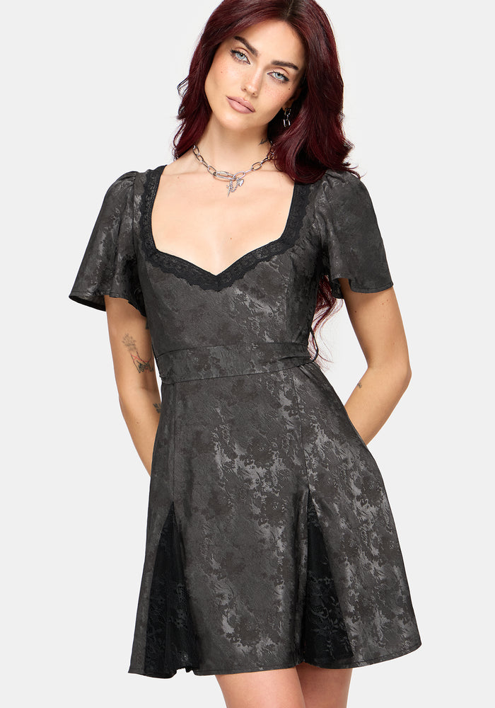 A woman modeling a short-sleeved black lace dress with a sweetheart neckline and black lace trim, set against a plain light gray background.