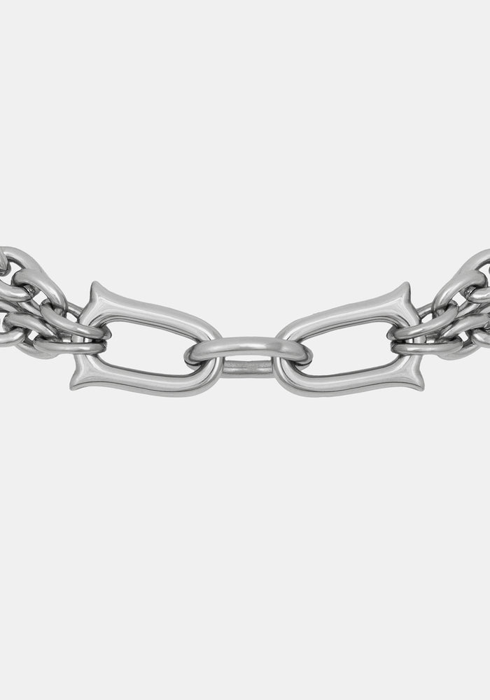 A close-up of a polished silver-toned metal chain with elongated oval links and decorative curved ends, shown against a plain light gray background.