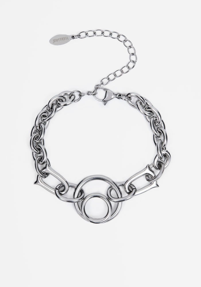 A silver-toned chain bracelet featuring a central interlocking circular link motif and an adjustable extender chain with a branded tag, shown on a light gray background.