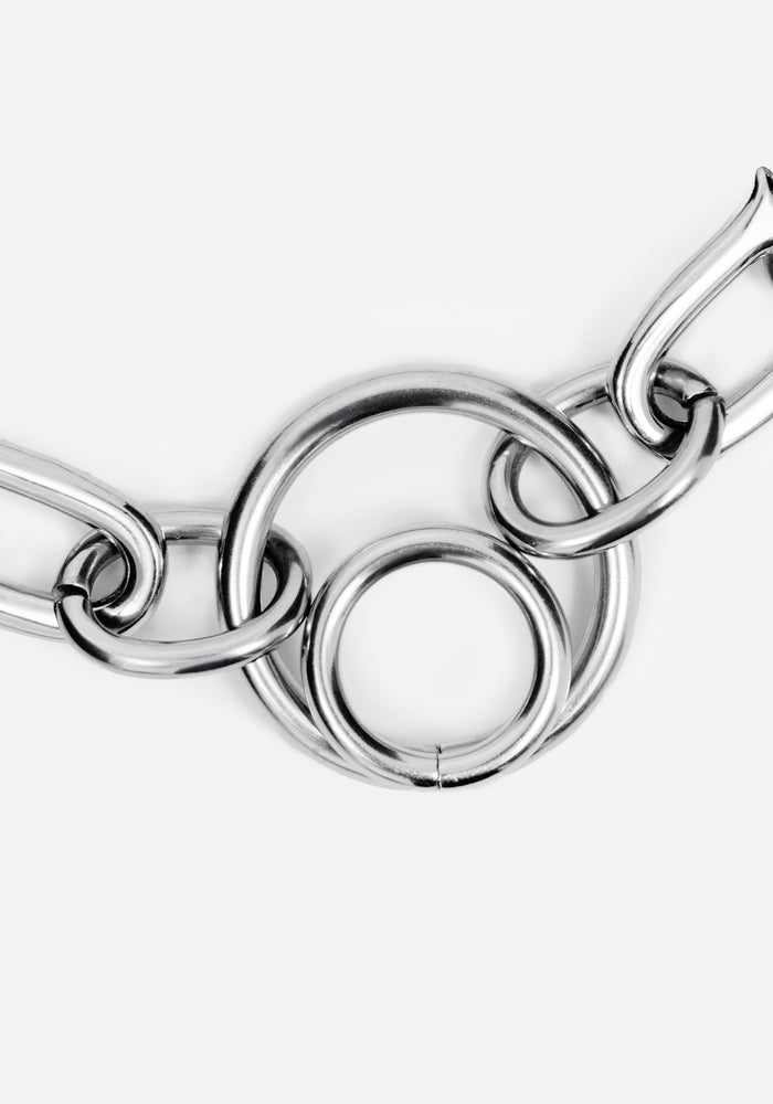 A close-up of a polished silver-toned metal chain with interlocking circular and elongated links on a plain light gray background.