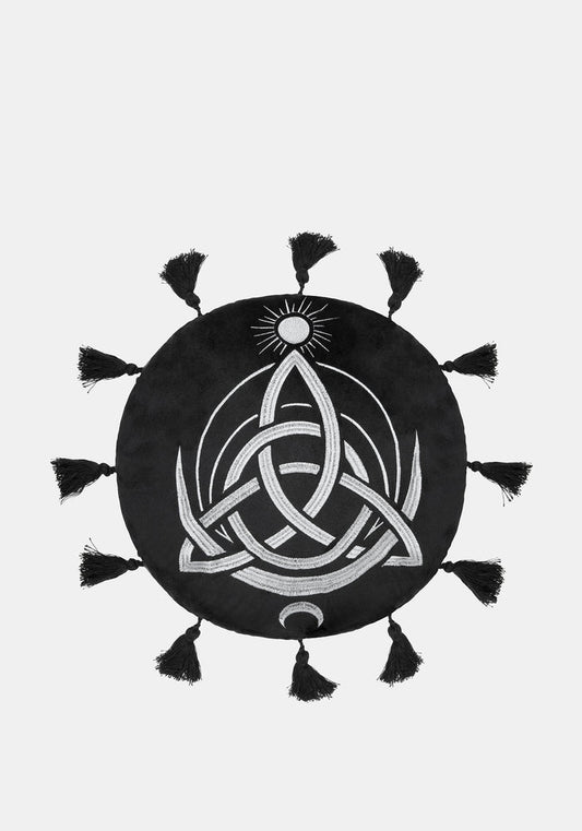 A circular black cushion with a white Celtic knot triquetra design, a small sun motif at the top, and tassels extending from the outer edge, shown on a light gray background.