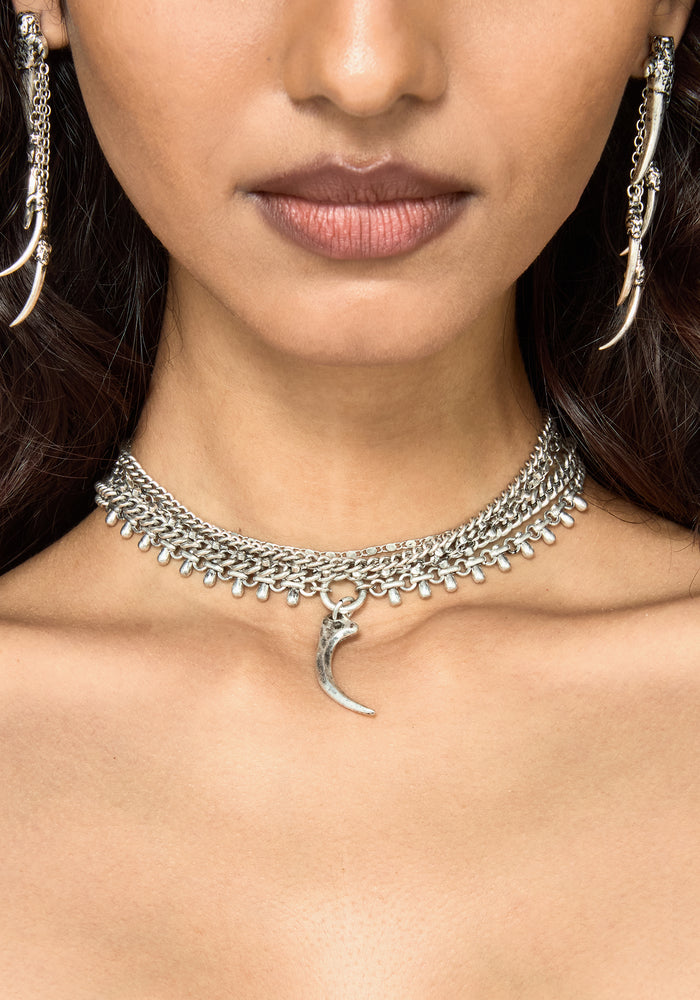 A close-up of a model wearing a silver-toned chain choker necklace with a crescent moon pendant, along with matching long dangling earrings.