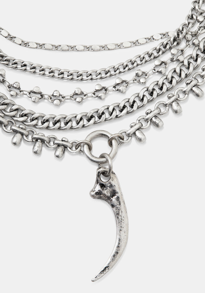 A layered silver-tone chain necklace featuring multiple textured chains, small skull-shaped links, and a curved claw or fang pendant, shown on a light gray background.